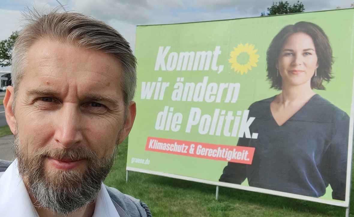 Norbert Schulze vor einem Wahlplakat der Grünen mit Annalena Baerbock. Text: Kommt, wir ändern die Politik. Klimaschutz & Gerechtigkeit